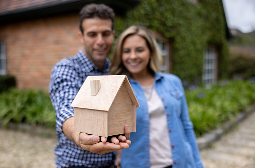 Happy Latin American couple holding a house model and smiling - real estate concepts