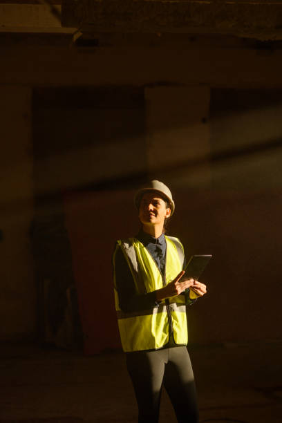 istock Female Architect indoors on Construction Site with sun beam falling on dust with PPE on tablet 1498704959