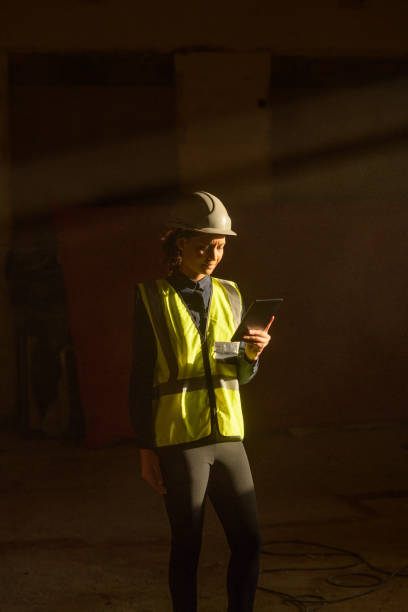 istock Female QS indoors on Construction Site with sun beam falling on dust with PPE on tablet 1498705014