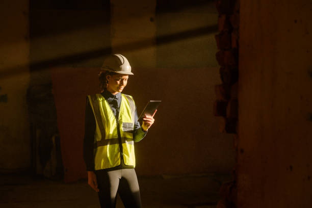 istock Female Worker indoors on an Construction Site with sun beam falling on dust with PPE on tablet 1498705059