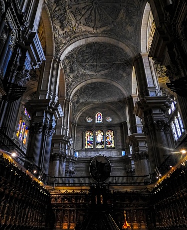 An interior view of the grand Cathedral of Malaga, Spain, featuring a high-arched ceiling and stained-glass windows
