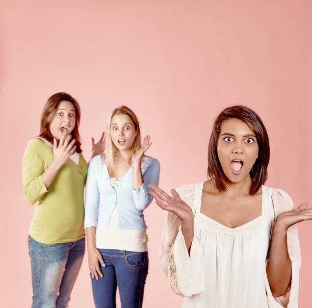 Three young female friends throw up their hands, mouths open, as they hear something surprising or shocking.
