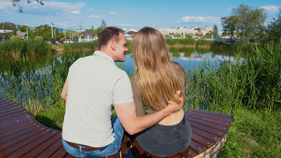 Man embraces the woman while they are sitting on a bench by the lake in the park
