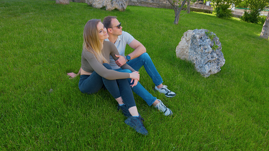 Man and woman are sitting on the green lawn,looking to the side