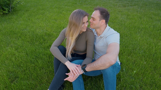 Man leans in to kiss the woman while sitting on the meadow