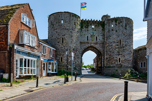 Rye, United Kingdom - Jun 13, 2023: The Landgate in Rye, East Sussex, England, a 14th century fortified gateway in the town walls standing on East Cliff. At one time there were four gates with Landgate being the only one to open on to dry land. An antique shop takes advantage of the fine weather to display its wares on the cobbled pavement.