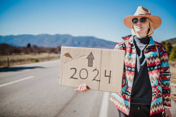 jusqu’en 2024. femme faisant de l’auto-stop seule et tenant une pancarte en carton - voeux 2024 photos et images de collection