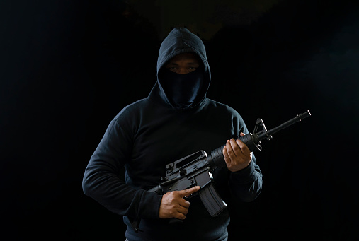 robber in black hoodie holding M16 gun on dark background