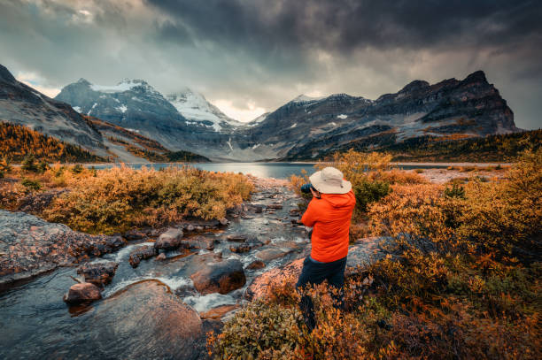 Travel photographer man taking a photo with camera at mount assiniboine in autumn wilderness by lake magog on moody day stock photo