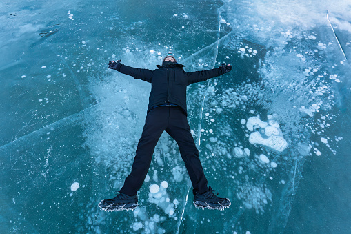 Young male tourist lying and enjoying outstretched arms on frozen lake with natural bubble in Abraham Lake on winter at Canada