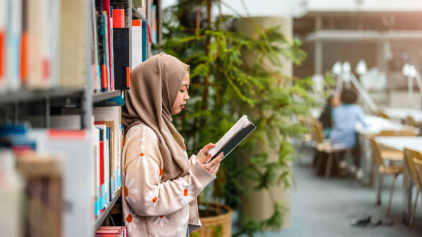 Young asian muslim woman reading book in a library
