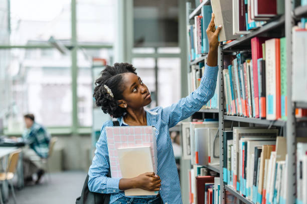 istock Black female student picking book from bookshelf in library 1498726083