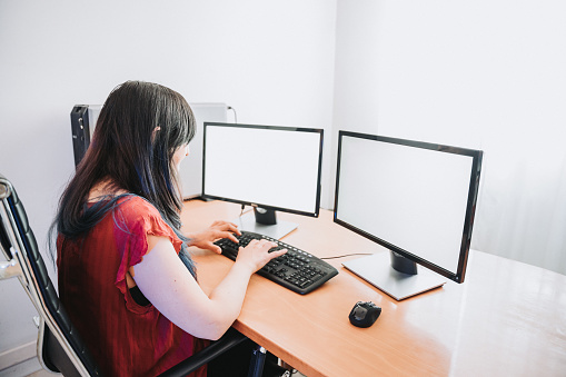 long black haired woman working with two monitors in office
