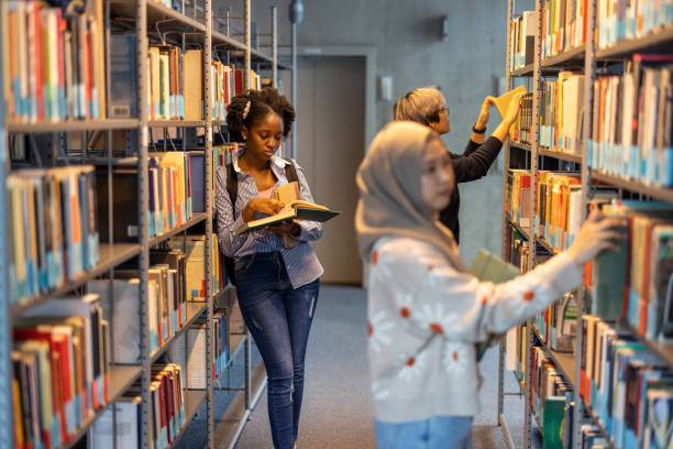 Portrait of a smiling young woman standing between bookshelves in the library