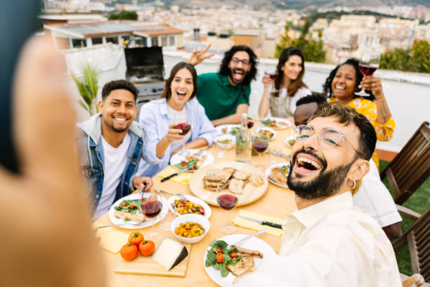 Happy young group of multiracial friends enjoying barbecue dinner on rooftop stock photo