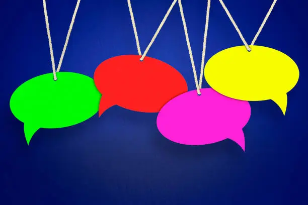 Photo of empty, colored speech bubbles hanging on a thread on a blue background