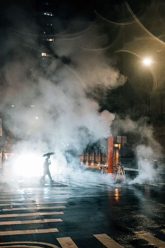 Pedestrian crosses street under the rain in New York City at night