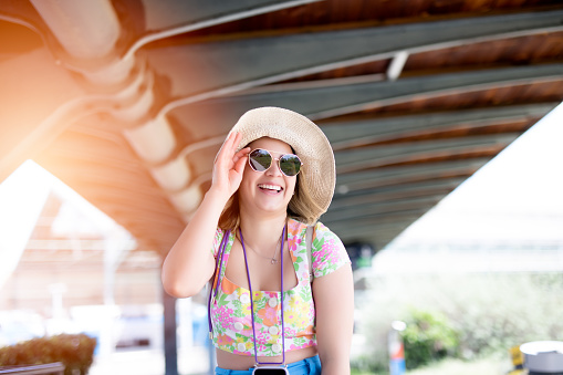 Happy young woman with sunglasses and hat at train station.