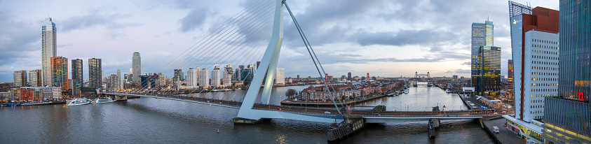 Rotterdam The Netherlands on December 7, 2022: Rotterdam skyline at sunrise from a cruise ship docked in the port. One of Holland’s most famous bridges, the Erasmus Bridge spans the River Nieuwe Maas and forms an important connection between the northern and southern parts of Rotterdam.