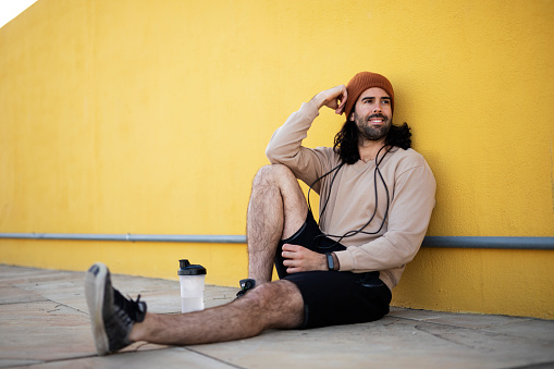Young athlete man sitting on the floor, resting after training. Happy man training outdoors.
