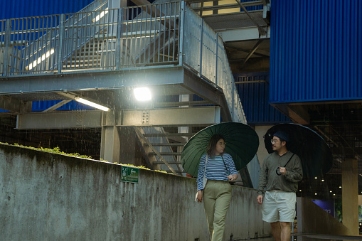 Asian couple having a romantic walk on rainy day. It's very rain. They are laughing and talking, the guy is holding umbrella.