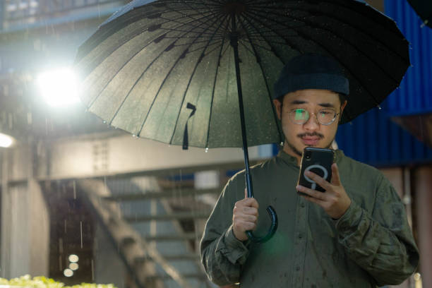 雨の中を外を歩きながら電話を使い、傘を持つ若い男 - concepts airport ideas watching ストックフォトと画像