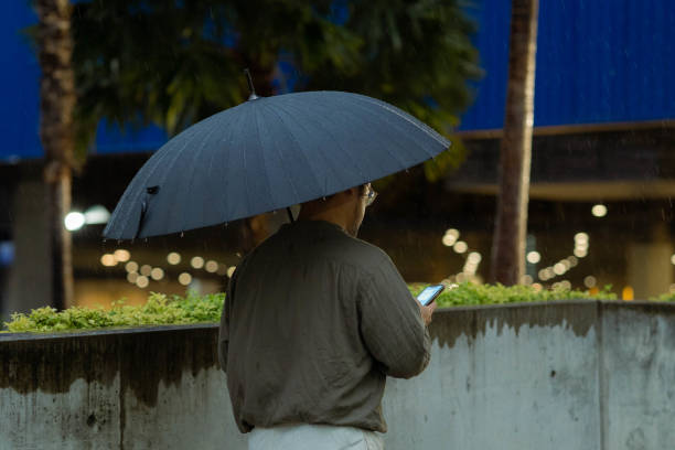 雨の中を外を歩きながら電話を使い、傘を持つ若い男 - concepts airport ideas watching ストックフォトと画像