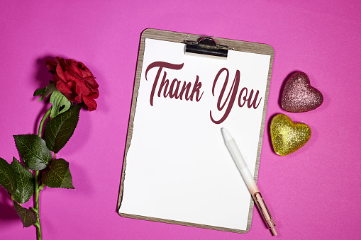 Thank you concept on clipboard with red rose flower and glitter hearts on pink background