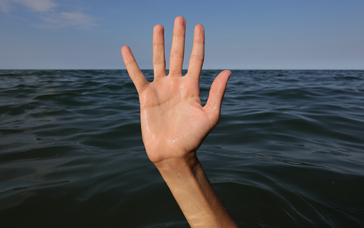 hand of man asking for help while in danger of drowning in the middle of the ocean water