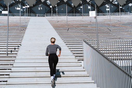 Woman athlete wearing female sportswear running and  exercising on staircase between bleachers of outdoor stadium.