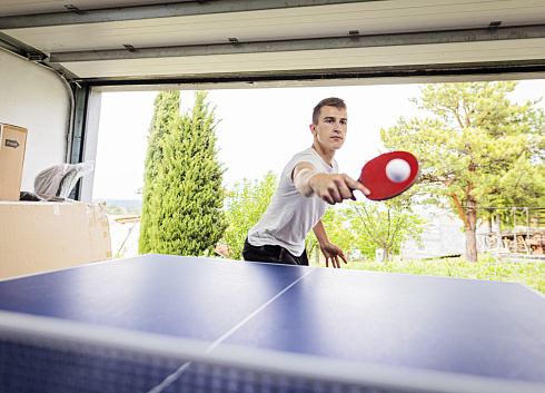 Low angle side view of young male in casual clothes playing ping pong