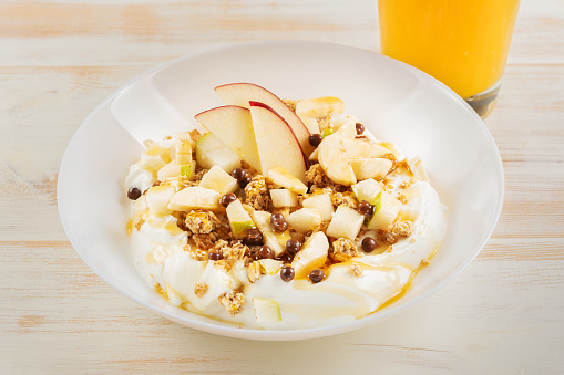 Îreakfast concept. Yogurt with flakes, fruits and juice on white wooden background.