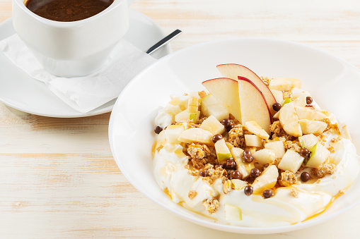 Yogurt with flakes, fruits and cup of coffee on white wooden background. Îreakfast concept.