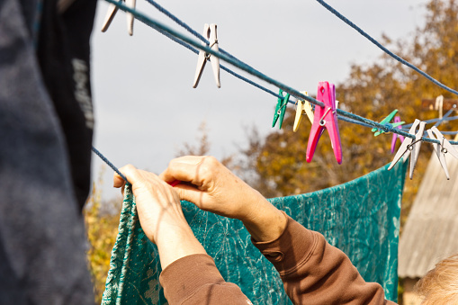 Laundry woman hangs clean wet cloth on clothes dryer after washing at home. Household chores and housekeeping