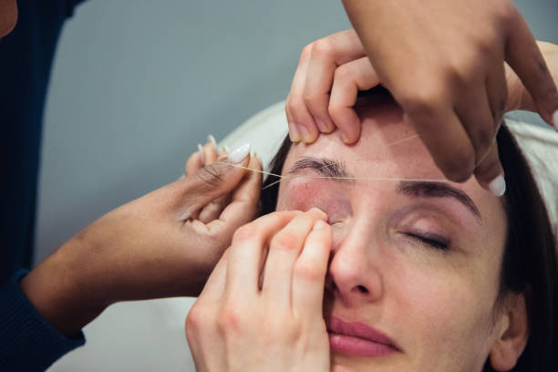 istock Caucasian woman removing hair from eyebrows with thread technique done by eyebrow stylist. Threading. Process Steps. Close up 1498770683