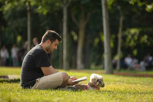 Young man is sitting on the grass with his dog at public park.