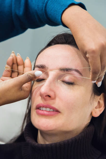 istock Caucasian woman removing hair from eyebrows with thread technique done by eyebrow stylist. Threading. Process Steps. Close up 1498770837