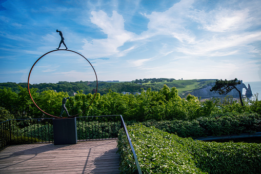 05-17-2023 Etretat ,  France.  Metal composition with small statues  in Etretat gardens and bamboo trees and famous cliff of Etretat  Falaise d'Avaln in right corner