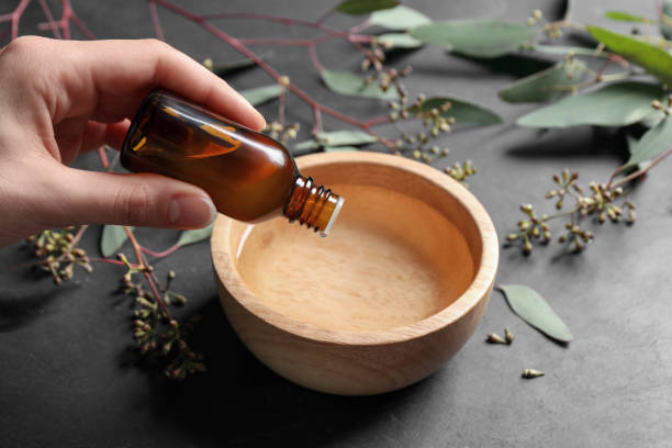istock Woman dripping eucalyptus essential oil from bottle into bowl at grey table, closeup 1498774968