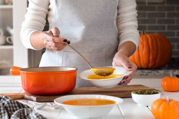 Woman using ladle to pour pumpkin soup into bowls in a kitchen