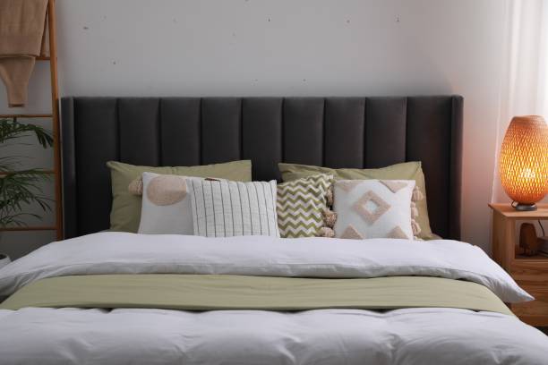 istock Comfortable bed with cushions, lamp on wooden bedside table in room. Stylish interior 1498776422