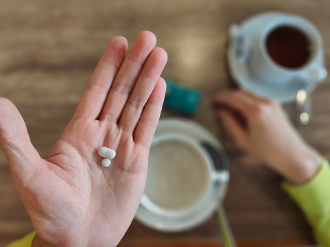 An Asian woman's palm with medicine with porridge, pill box and hot tea on table