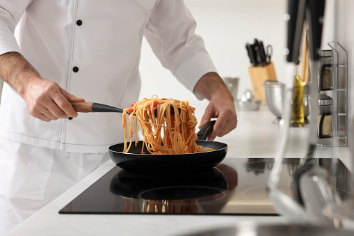 Professional chef cooking delicious pasta on stove in kitchen, closeup