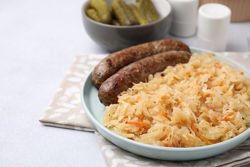 Plate with sauerkraut and sausages on light grey table, closeup. Space for text