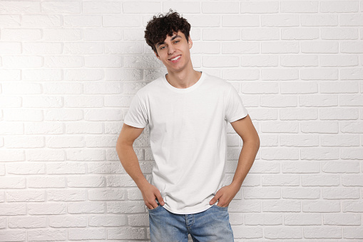 Man wearing stylish t-shirt near white brick wall. Mockup for design