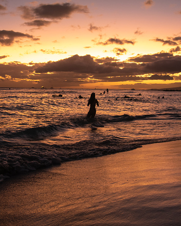 Incredible sunset at Waikiki Beach, Hawaii, USA. One womans silhouette standing in water.