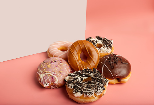 a selection of various doughnuts in front of a white box in a pink background