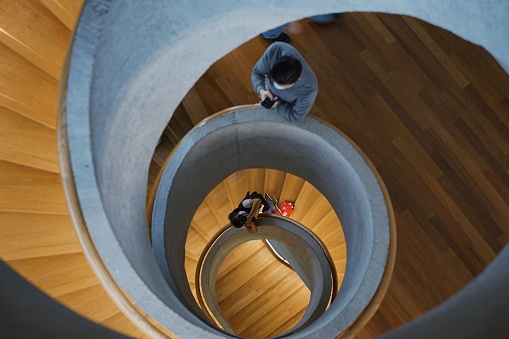 A young female photographer stands on a spiral staircase, looking through a camera lens