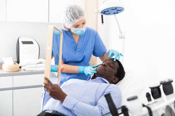 istock Man looking at mirror while beautician examining his face in cosmetology office 1498797337