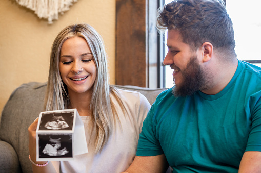 Happy young couple look at ultrasound photos and smile while celebrating pregnancy